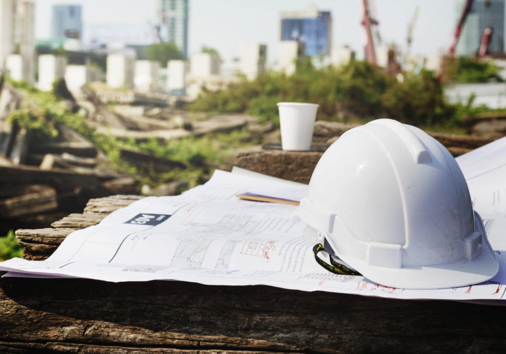 Bauhelm und technische Baupläne auf Baustelle einer Neubauimmobilie