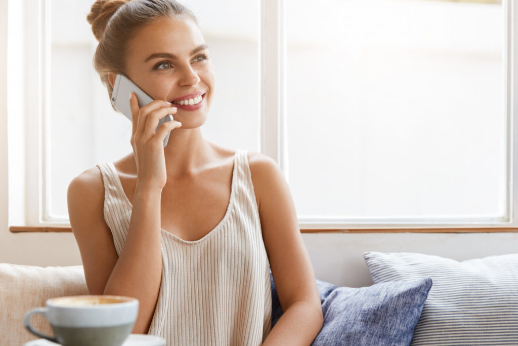 Glückliche Tippgeberin bespricht Immobilienverkauf telefonisch im Wohnzimmer