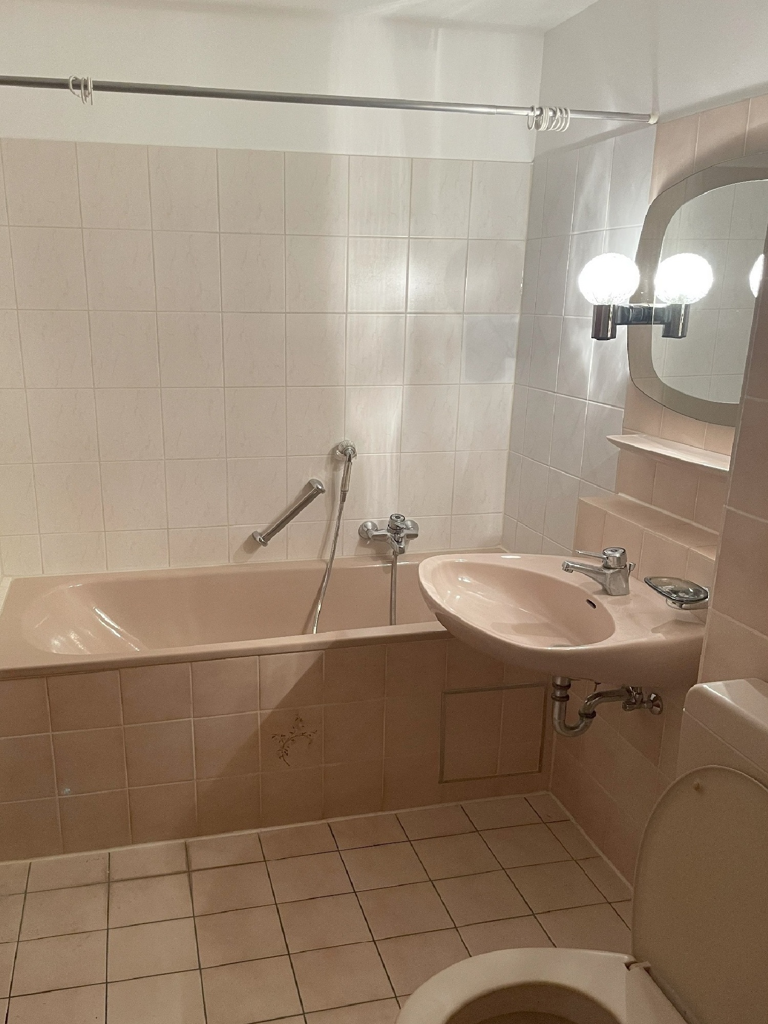 Badezimmer vor der Sanierung mit Badewanne, Waschtisch und Spiegel, beige-rosé Fliesen und Kugelleuchten